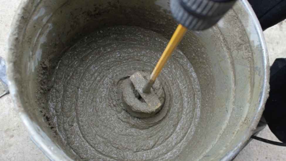 Close-up realistic photograph of a person thoroughly mixing concrete inside a five-gallon bucket, showing the correct thick workable consistency, concrete paddle or hand tool visible, detailed texture, natural lighting, no text.