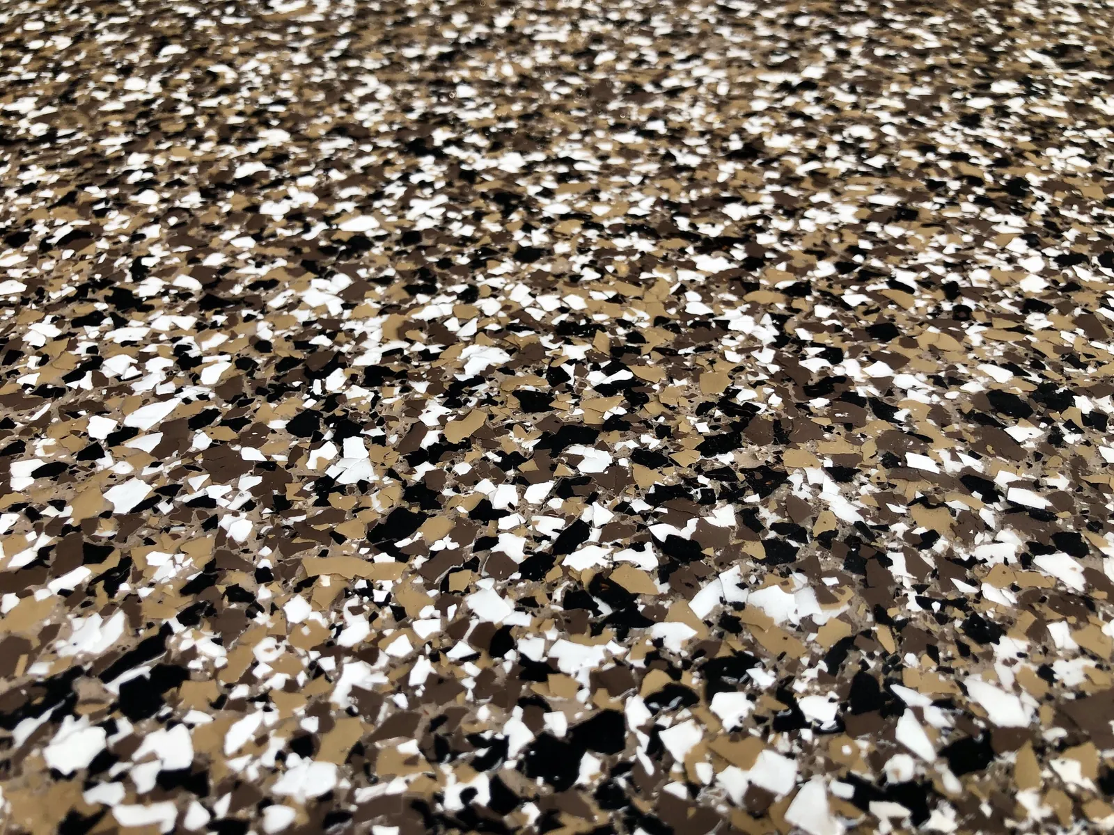 Close-up of epoxy base coat with vinyl chips being sealed on a garage floor